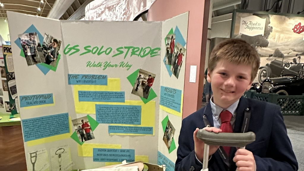 An Iowa student named Gavin standing with his invention and display board at nationals